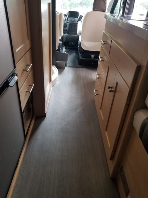Standing at the rear of the RV looking towards the cockpit.  To the left is the fridge, wardrobe closet, and drawers for storage.  To the right is the kitchen area.