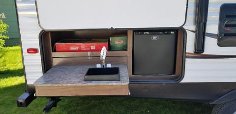 Outdoor kitchen with hot/cold water, mini fridge, and coleman stovetop.