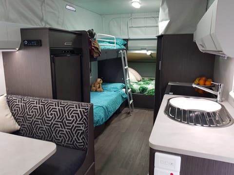 Two bunk beds in the middle with a double bed at the back. Large fridge opposite gas cooking area and sink with hot water