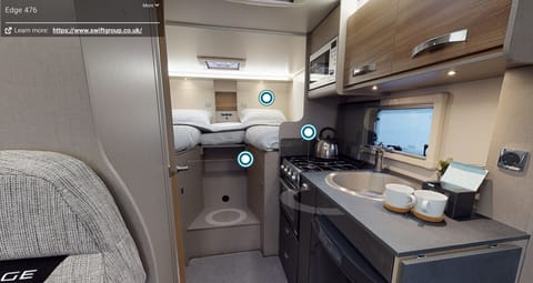 Rear view of the motorhome showing larger double bed and the spacious kitchenette, complete with oven/grill/hob,  microwave and fridge/freezer. 