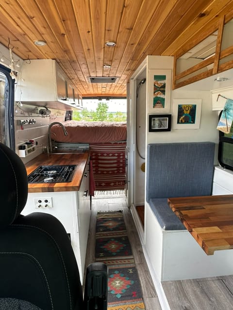 Views of the dining area, kitchen, cabinets, shower, and sleeping area with the back doors open, showcasing the spacious and well-designed interior.