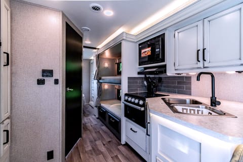 The kitchen area with a sink and 3-burner stove top, complete with a small oven, is a fully functional culinary space designed for cooking and meal preparation on the go. 
