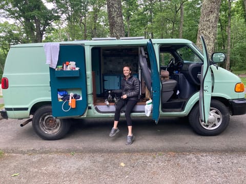 The "bathroom" is on the left, featuring space for toiletries and towels, and our electric camp shower. No toilet in van. GF and dog not included. 