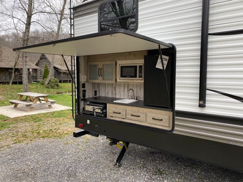 Outdoor mini fridge, microwave, and grill with sink and storage space.