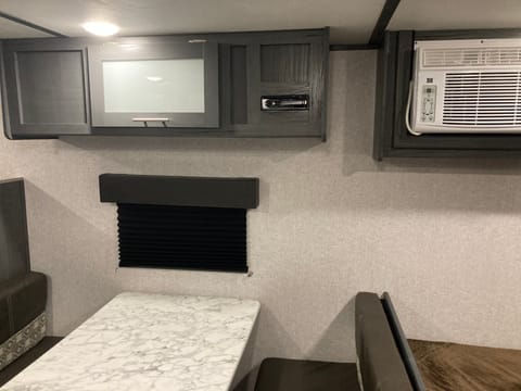This photo shows a window by the dining area, overhead storage, radio with Bluetooth, aux, cd and radio capacity and the AC unit.