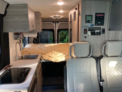 This is looking back at the inside of the van from the front cab. You see the 3rd and 4th seats, the kitchen (left) and the queen size bed in the back