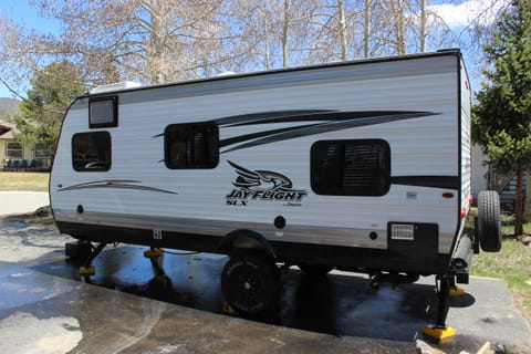 Rear left quarter shows the windows for the queen bed, kitchenette, and lower bunk. Also the four corner stabilizing jacks.