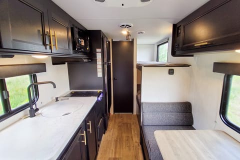 Interior image showing booth dinette, kitchen sink, cooktop, and single bunks.