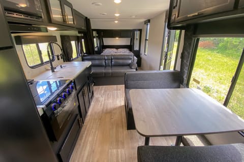 Interior image showing booth dinette, cooktop, oven, kitchen sink, couch, and queen bed