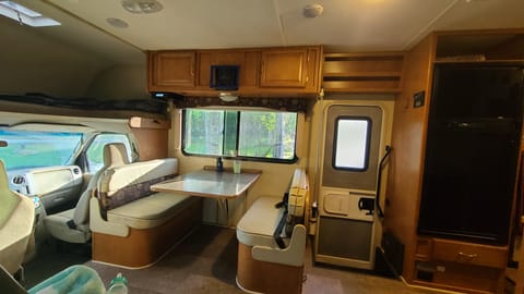 Dining table near door with 3 seatbelts. Small TV mounts above table, usually when the RV is parked.