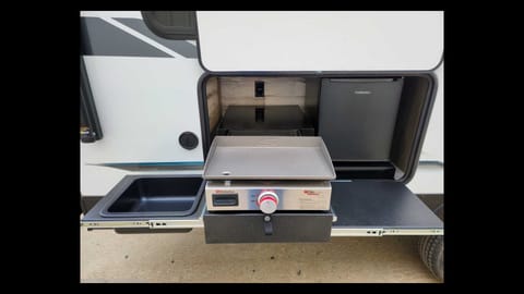 Outdoor kitchen includes a griddle, mini-fridge, waste basin, extendable hose (not pictured), and counter space.