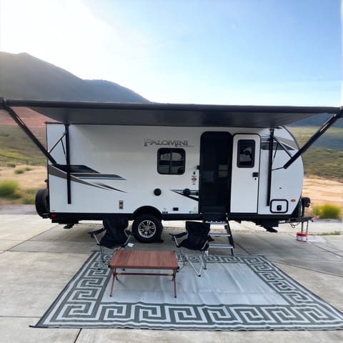 Main entrance of trailer with 15 foot power awning extended, area rug, table, and two camping chairs. Contact your host if you need additional chairs.