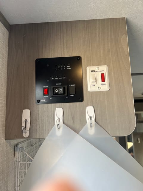 Control panel for water pump, hot water, monitor black & gray water as well as power awning controls. Hanging items are plastic cutting boards.