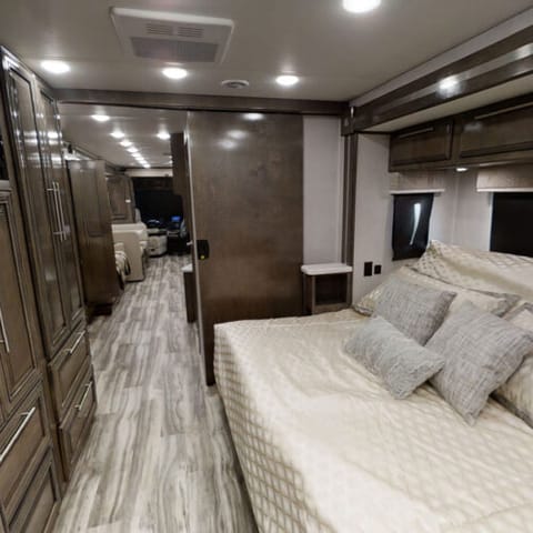 This Class A RV has a cozy retreat, complete with a memory foam mattress that cradles you in comfort. Imagine a day bed that transforms with your needs. After a day filled with adventure, you can prop it up, sit back, and lose yourself in your favorite TV show. 

Simply flick a switch and the bed descends, ready to lull you into a peaceful slumber. The beauty of this bed is not just in its versatility, but also in the freedom it gives you. When it's not in use, it tucks away, leaving you with ample space to move around at ease. 

Above the bed, you'll find ample storage complete with convenient outlets. And for your comfort, both sides of the bed feature USB ports. The solid surface countertops serve as nightstands.