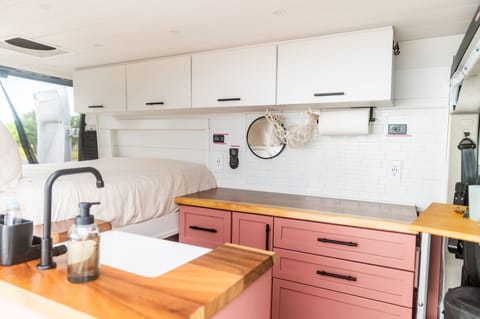 A beautiful pink interior with a bed in the back, kitchen and bathroom in the middle, and dining up front.