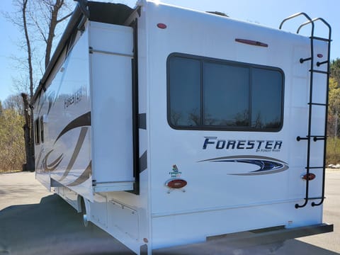 This RV has a trailer hitch towing package and a roof ladder. The slide out is fully extended and does not take up much side space.