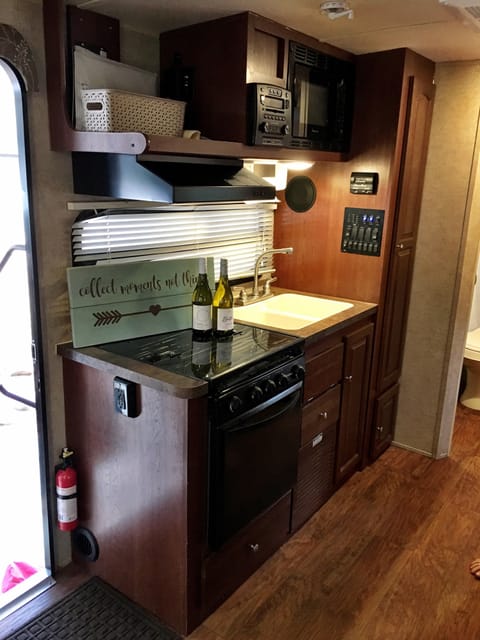 Camper kitchen with oven, 3 burner cook-top, large sink, microwave, tall 4 shelf pantry and (not pictured) fridge and freezer.  Fully stocked with cups, utensils, plates, bowls, cookware and serving ware.