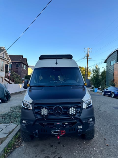 The van features LP9 driving / spot lights, BD Squadra Pro ditch lights, a CA Tuned front crash bar with integrated Warn winch, and protective covering on the hood + lights. 