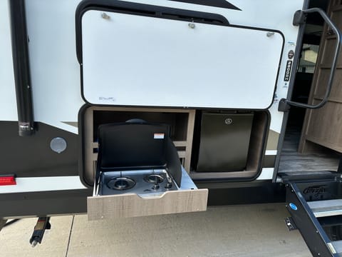 Outdoor kitchen complete with Mini Fridge. The refrigerator does not operate while the camper is in motion. Camper must be hooked up to a power source. This a wonderful functional way to store your beverages. For easy access while enjoying the great outdoors.  Atop the stove is storge for your outdoor cooking supplies as well as a cold water connection here for your convenience. 