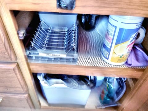 Lower Cabinet Below Double Sink Contains Dish Drying Rack, Trash Can and Cleaning Supplies