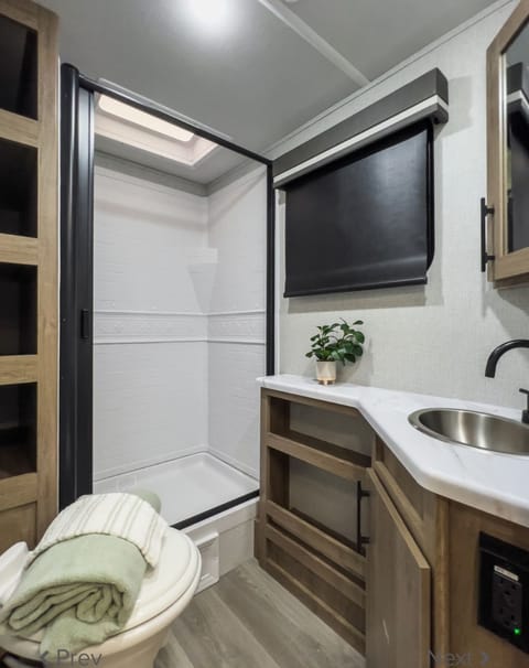 Bathroom, which features a full-size shower with a privacy sliding panel, storage, and a regular-size toilet. With an onboard tankless water heater, you will enjoy nice, long, warm showers during the chilly months. 