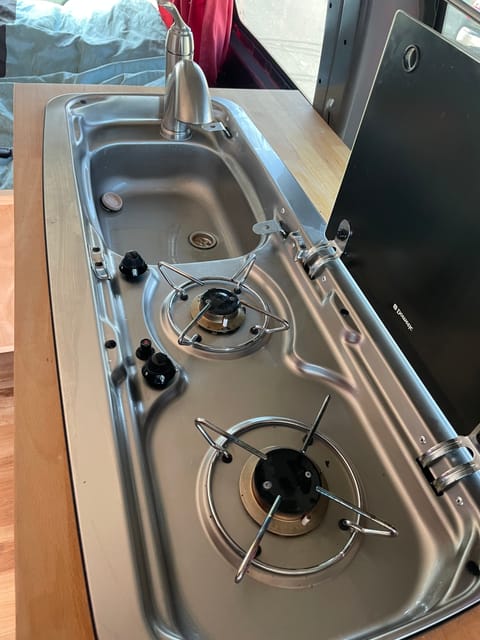 Two burner propane stove, sink with interior 10-gallon storage tank for grey water. Propane tank attached under vehicle.