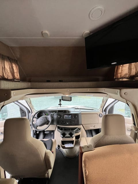 This pic covers both the driver's seats, and the overhead queen bed.  There is a panel that covers the driving area.  Side windows, USB chargers and the living area TV access. There are USB charges near the bed, and cup holders.

Note: There is no rear view mirror, but there is a screen and that's for the rear mounted camera and lane-change cameras.

Note 2: The dash-mounted radio has some tech we haven't figured out. And there is a whole media control system and roof antenna as well. 