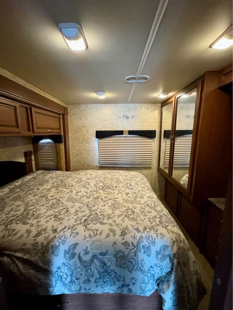 Queen sized memory foam mattress with reading lamps by headboard, overhead storage cabinets. There is a wardrobe closet at the foot of the bed as well as six drawers and a TV with Blu-ray player.