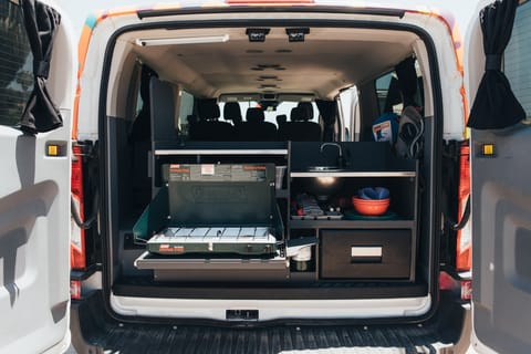 The camper van comes with a kitchen equipped with a tow-burner propane stove, sink, overhead light, and solar-powered fridge