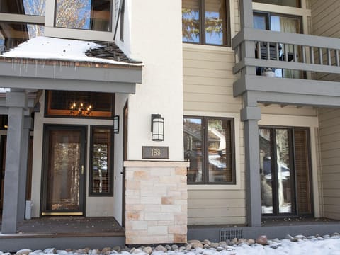 Exterior view of a two-story building with snow on the ground, showcasing wooden architectural details, a chandelier visible through the front glass door, and the number "188" displayed beside the entrance.