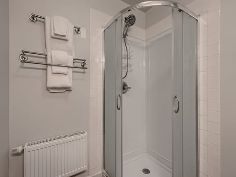 A clean, modern bathroom with a corner glass shower, tiled walls, a heated towel rack holding white towels, and a white radiator below.