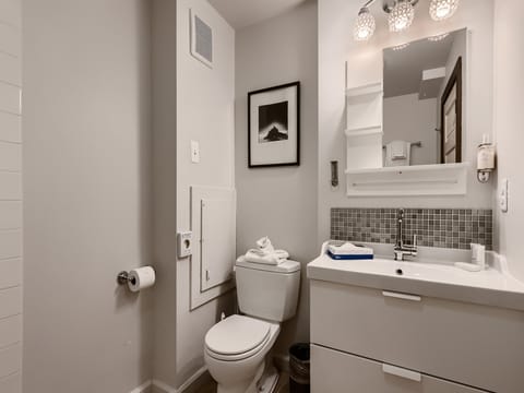 A small bathroom featuring a toilet, a sink with a cabinet, a framed picture on the wall, a toilet paper holder, and a towel neatly folded on the toilet lid.