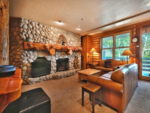Spacious living room with feature river stone fireplace wall, flat screen TV, and stunning single log mantle