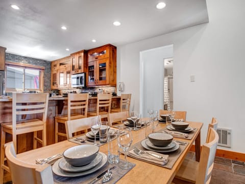 Wooden table with 6 wood chairs, perfectly set with 6 place settings, situated next to the open concept kitchen.