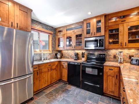 Warm wood cabinets with undermounted lighting, black dishwasher and oven, stainless microwave and fridge and warm toned tile.