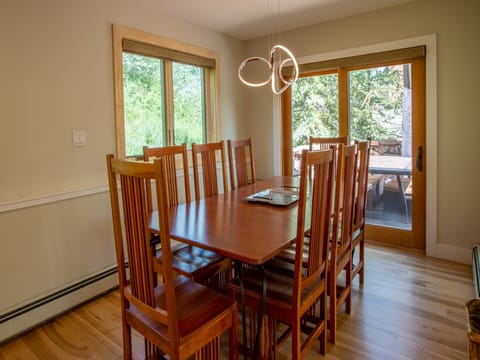 A dining room with a rectangular wooden table, eight wooden chairs, a modern light fixture, and a sliding glass door leading to a patio.