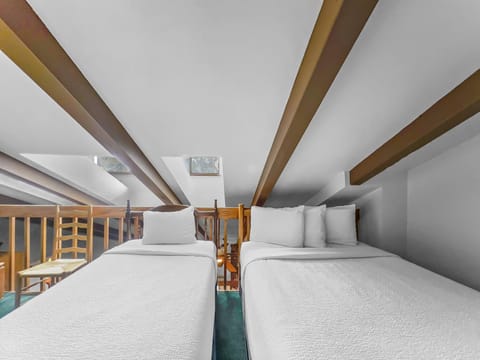 Two neatly made beds under wooden beams in a loft-style room, with skylights providing natural light.