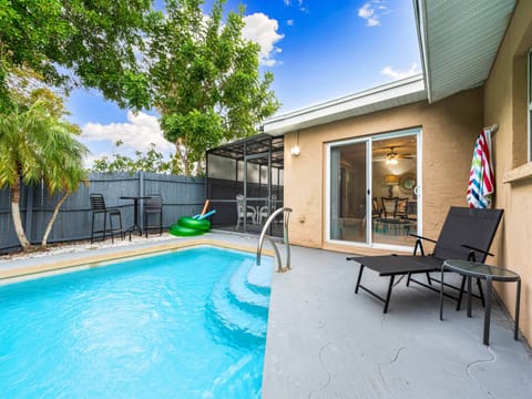 A backyard pool area with a small pool, two lounge chairs, a sliding glass door leading indoors, and a fenced perimeter. Pool floats and outdoor furniture are visible in the background.