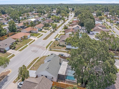 Aerial view of a residential neighborhood featuring single-family homes with backyards, tree-lined streets, and intersecting roads on a sunny day.