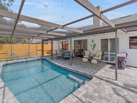 A screened-in backyard pool area with patio furniture, a covered section, and a view of a basketball hoop in the adjacent lawn area.