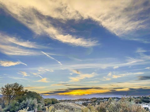 A scenic sunset with a sky filled with wispy clouds above a landscape of trees and distant hills.