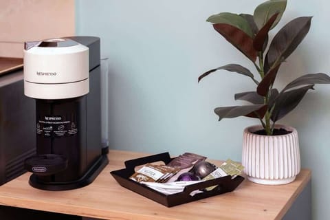 A neat coffee station featuring a black coffee machine, mugs, and a small potted plant, creating a welcoming spot for a morning brew.

