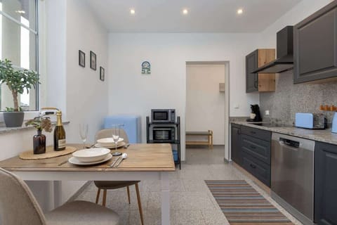 An open-plan dining area next to the kitchen, showcasing dark grey cabinets, a small round dining table, and warm wooden accents.

