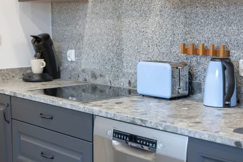 A kitchen countertop with speckled stone tiles, equipped with a dishwasher, toaster, kettle, and a convenient knife block, blending functionality with style.

