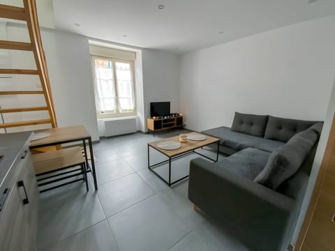 "In this living room you will find a welcoming and modern atmosphere. A comfortable corner sofa invites you to relax, ideal for relaxing while watching TV, which is placed in a corner of the room. A large window lets in natural light, offering a bright and pleasant atmosphere.A practical coffee table is in the centre of the room, perfect for snacks or drinks. The white walls add a touch of freshness and brightness, while the grey tile adds a contemporary touch to the entire room. It is a friendly and comfortable space to relax and spend time with family or friends."