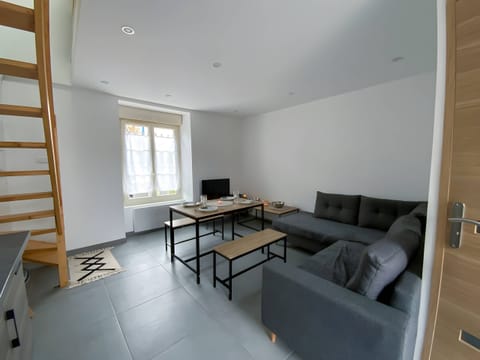 "In this living room, you will discover a convivial and modern space. A comfortable corner sofa is arranged for optimal relaxation. Television is strategically placed for moments of entertainment.A large window illuminates the room by letting in natural light. A dining table is present, ideal for meals with family or friends. The white walls offer a light and clean atmosphere, while the grey tiles add a contemporary touch to the whole. It is a perfect place to get together, relax and enjoy good times together."