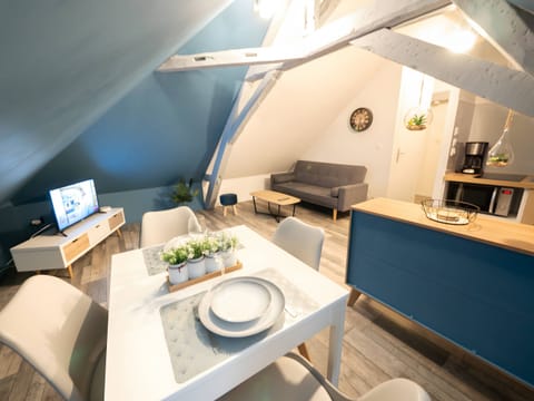 "This attic space combines dining room, kitchen and living room. Gray beams on the ceiling for a rustic charm. Blue wall for a focal point. TV area dedicated to entertainment. Comfortable and elegant to relax and share meals. Bright with sofa and coffee table."