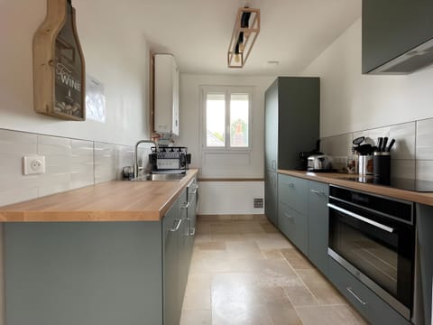 "Discover L'Enchantement's refined kitchen: gray furniture, beech worktop, double window and a stunning white rack."