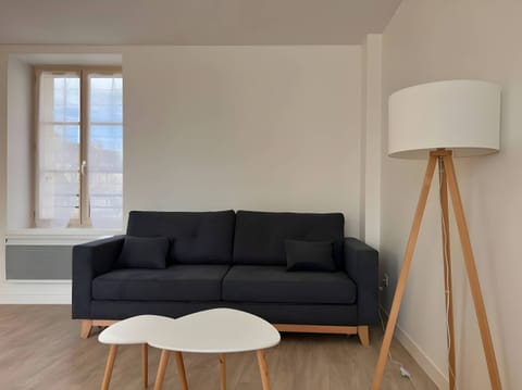 "Discover the spacious living room of the apartment "Le Donjon" with its floor lamp, comfortable sofa, coffee table and a window letting in natural light. Enjoy a warm and inviting space to relax and spend pleasant moments."