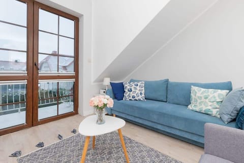 A cozy living area with blue sofas, nautical-themed pillows, and a coffee table, complemented by natural light from large windows.
